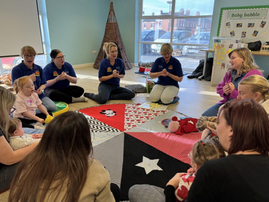 A group of parents, babies and toddlers, including children with Down syndrome, participating in a Signing for Babies session.